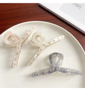 Close-up of pearlized acetate hair claws with rhinestones in pink, beige, and blue
