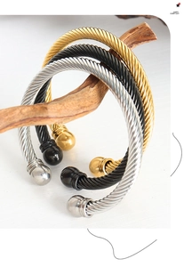 Dettaglio di bracciali a fune in acciaio oro, argento e nero su supporto di legno