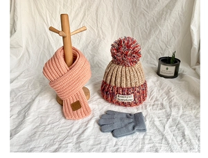 Close-up of pink knit scarf, beige pom-pom hat, and gray gloves for winter warmth