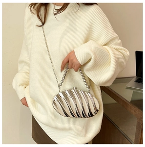 Detail of silver shell-shaped clutch with wavy texture and beaded handle on model