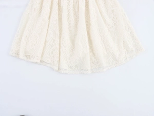 Detailed macro view of the intricate floral lace texture and wavy hem on a beige dress