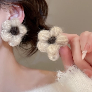 Close-up of knit flower stud earrings with soft beige wool petals and a glossy pearl drop