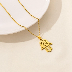 Detail of a golden Hamsa Hand pendant on a stainless steel necklace over a white plate