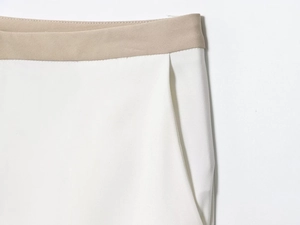 Detail of color-block waistband and side pocket on white straight-leg trousers