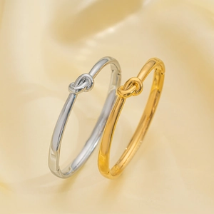 Minimalist knotted heart bracelets in gold and silver finish on yellow silk fabric