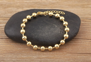 Detailed close-up of a 18k gold plated beaded bracelet on a dark stone background