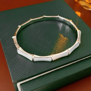 Detail view of gold-plated bamboo-style bangle with white shell inlay on green leather