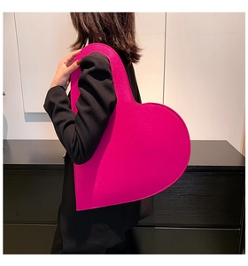 Detailed shoulder view of a large magenta heart-shaped felt handbag worn with a black blazer