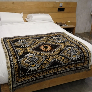 Detail of bohemian woven blanket with sun totem patterns and fringe edges on bed