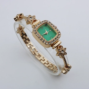 Detail of luxury gold bracelet watch with green rectangular dial and floral diamond accents