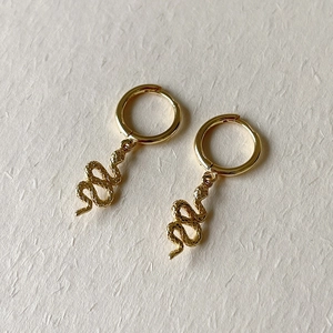 Detailed view of gold S925 sterling silver snake pendant hoop earrings on a beige background