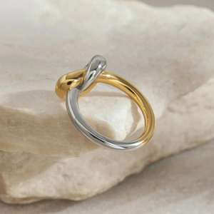 Detail of two-tone gold and silver interlocking rings on a textured stone surface