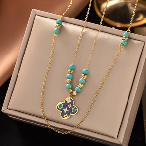 Detail of a gold titanium necklace with green beads and a purple clover pendant