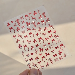 Detail view of 3D embossed red bow nail stickers with pearls and metallic accents