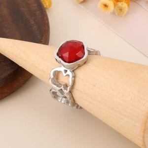 Close-up of a silver hollow flower ring with a red faceted gemstone on a wooden stand