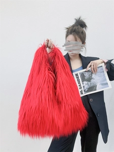 Detail view of a person holding a vibrant red long faux fur tote bag with a plush texture