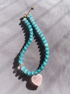 Close-up of blue cat eye beads with a pink heart pendant on a soft grey fabric