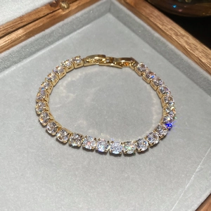 Detailed close-up of golden tennis bracelet with sparkling zircons on grey velvet background