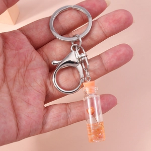Detail showing a mini glass wishing bottle keychain with an orange dried flower inside
