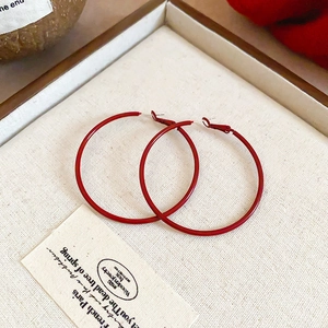 Macro view of large red enamel hoop earrings in a beige tray with vintage French card