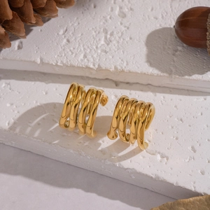 Detailed view of irregular geometric gold hoop earrings on natural stone with pine cones