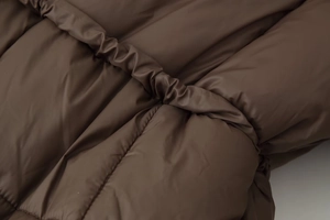 Gros plan sur la texture matelassée et le cordon de serrage à la taille de cette doudoune marron