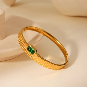 Detail view of gold stainless steel bangle with vertical stripes and green gemstone inlay