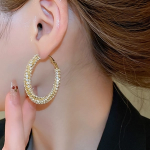 Close-up of a model wearing a gold twisted hoop earring with sparkling rhinestones