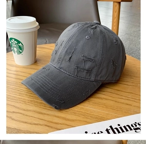 Detail of distressed dark grey baseball cap with torn fabric on a wooden surface