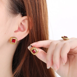 Dettaglio di orecchini e anello quadrati dorati con pietre preziose rosse su modella