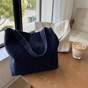 Dettaglio di borse tote in denim e tela con etichette laterali su tavolo di legno