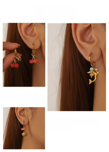 Detailed close-up of colorful enamel cherry and dolphin charms on golden hoop earrings