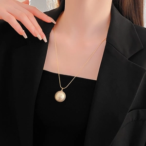 Detailed view of an elegant gold necklace with a large champagne pearl on a black blazer