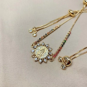 Nahaufnahme eines goldenen Armbands mit religiösem Anhänger und bunten Edelsteinen