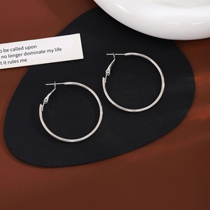 Minimalist silver hoop earrings placed on a black oval pad with soft lighting