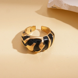 Close-up of gold and black enamel irregular wave ring on warm beige texture