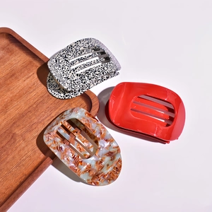 Three acetate hair claws in red, spotted, and amber patterns displayed on a wooden tray