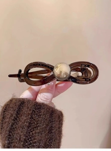 Detail of coffee-colored acrylic shark hair clip with infinity bow design and pearl accent