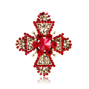 Close-up of golden cross brooch with red crystals and intricate openwork details
