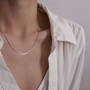 Close-up of minimalist silver snake chain necklace worn on neck with white shirt