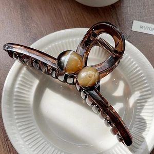 Detail of amber translucent hair claw clip with cat-eye beads on a white ceramic plate