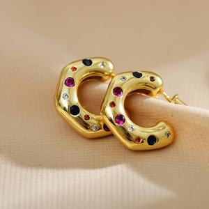 Macro shot of gold C-shaped hoop earrings with colorful inlaid gems on beige fabric
