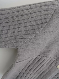 Detailed macro view of gray knitted sweater texture featuring an elegant pearl button