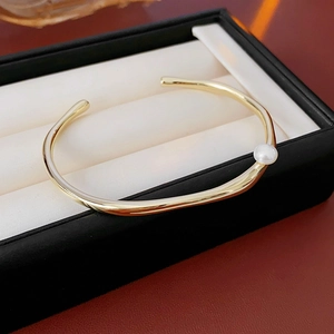 Close-up of golden geometric bangle with pearl accent in elegant jewelry box display
