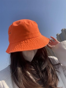 Close-up of bright orange sun hat worn by a model against a clear blue sky background