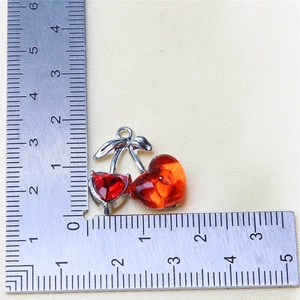 Close-up of red cherry jewelry pendant with silver leaves measuring 2.5cm on a ruler