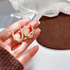 Elegant gold oval hoop earrings with polished metal finish held by hand on white surface
