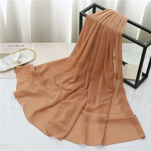 Detail view of caramel pearl chiffon hijab scarf draped on metal rack with luxury props