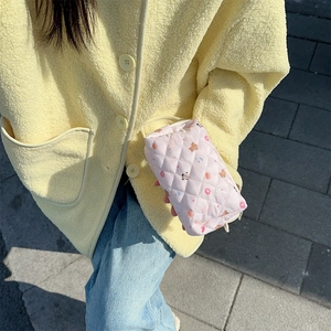 Detailed close-up of a pink quilted cosmetic bag held by hand in natural outdoor light