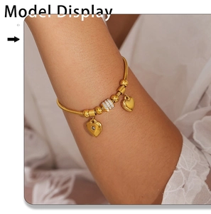 Detailaufnahme des goldenen Schlangenarmbands mit Herzanhängern und Zirkon-verzierten Perlen